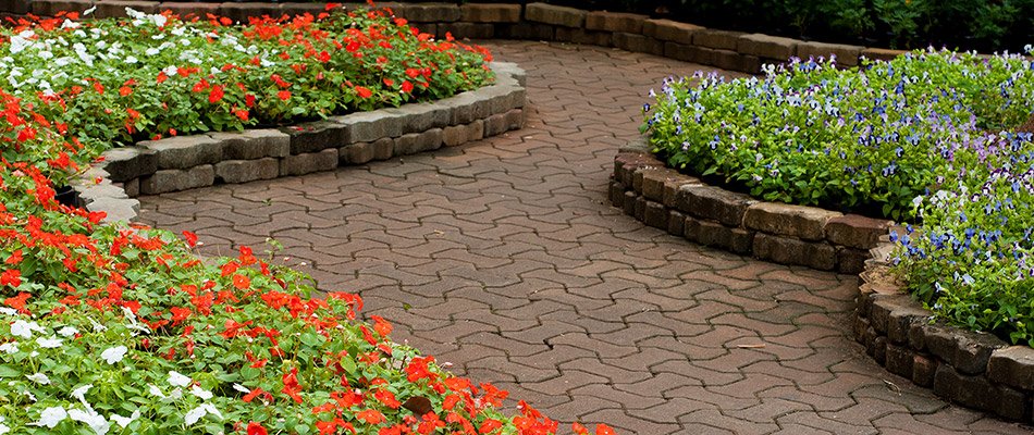 A brick paver patio with raised landscape beds filled with red and white flowers by a home in Notre Dame, IN.